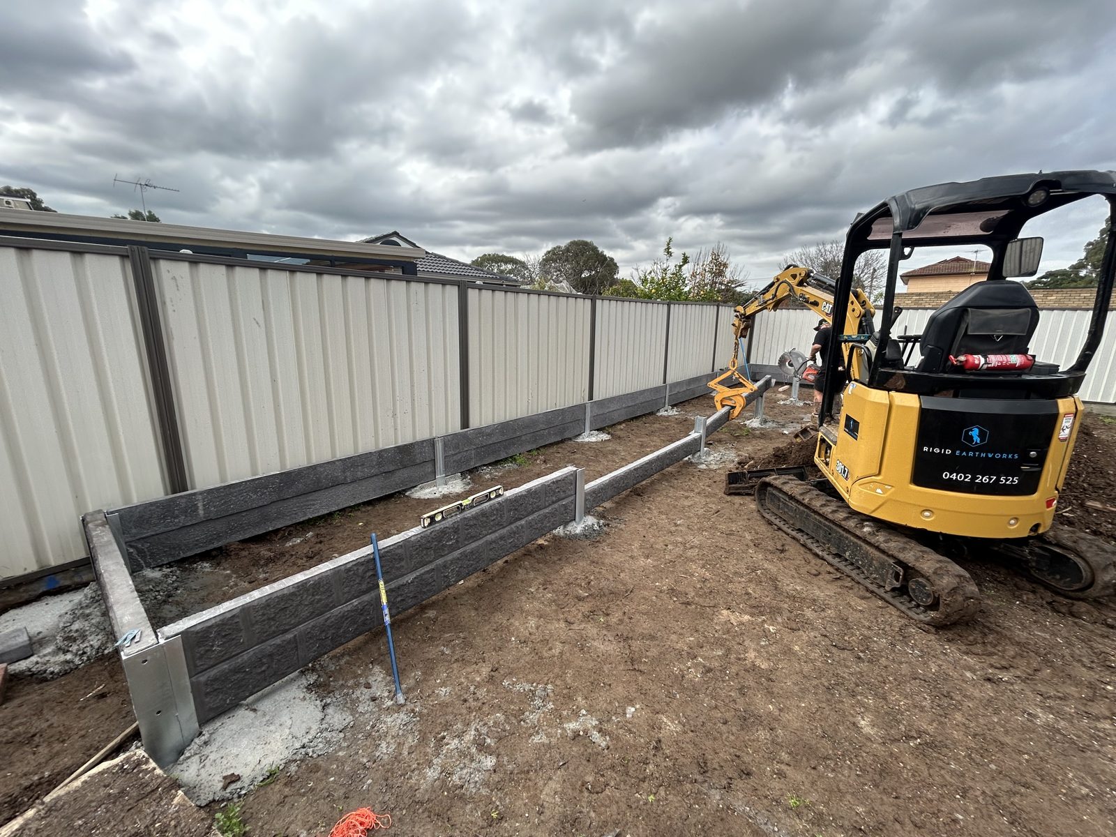 Rigid Earthworks excavator positioning a concrete sleeper between retaining-wall posts in St Albans